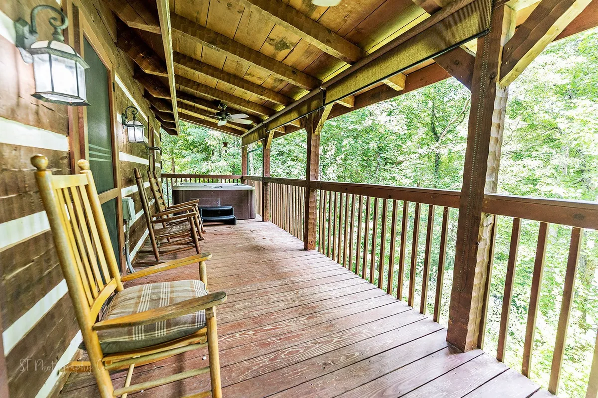 This image captures a wooden deck featuring inviting rocking chairs and a hot tub, all set against a lush, natural backdrop. The wooden railing and surrounding trees provide a sense of privacy and immersion in nature. The atmosphere is tranquil, perfect for enjoying both sunrise coffee and evening relaxation beneath the stars.