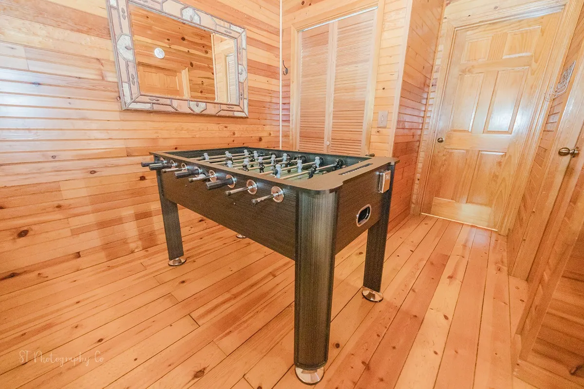 A foosball table stands out against rustic wooden walls and a homey mirror, inviting guests to gather for friendly matches and social moments in a cozy corner of the cabin.
