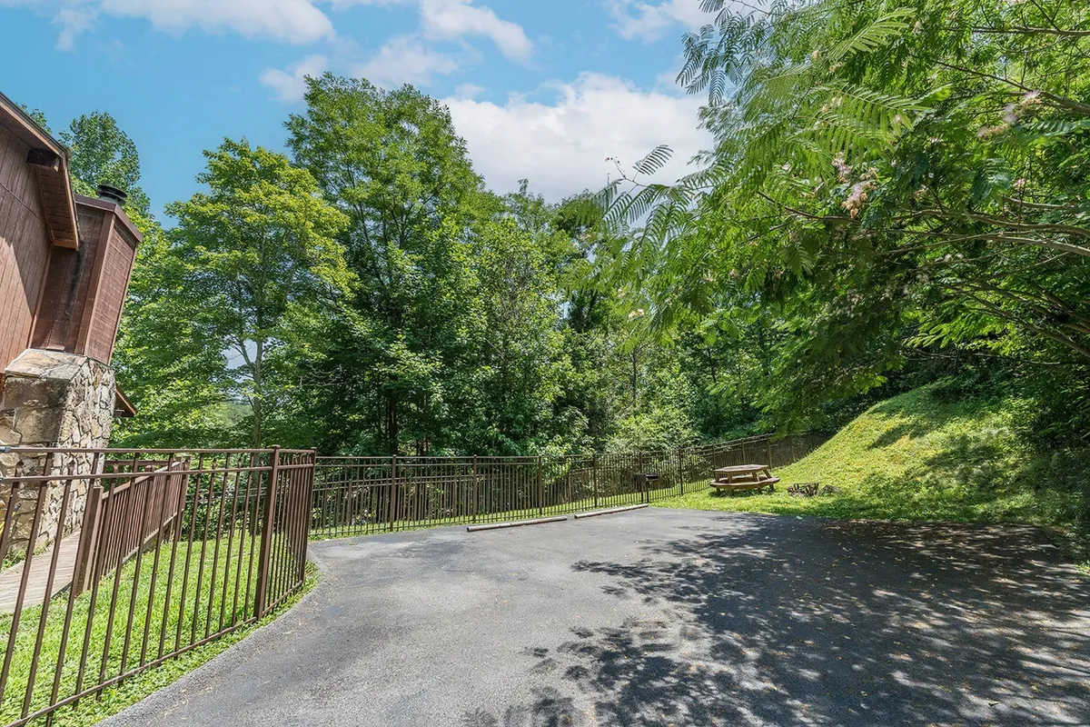 A view of a wooden picnic area nestled beneath a canopy of trees. The wooden railing frames the scene, inviting guests to enjoy picnics or relax outdoors while surrounded by greenery.