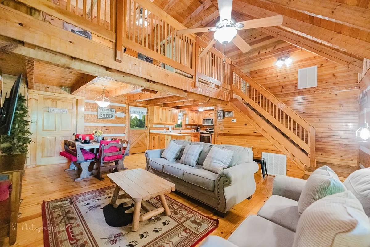 A wide view of the heart-of-the-home kitchen and adjacent dining nook, featuring rustic wooden beams, large windows bringing in natural light, a spacious dining table perfect for group meals or board games, and a kitchen area equipped for gatherings. The scene radiates warmth and togetherness, fitting for family and friends to connect over shared meals or activities.