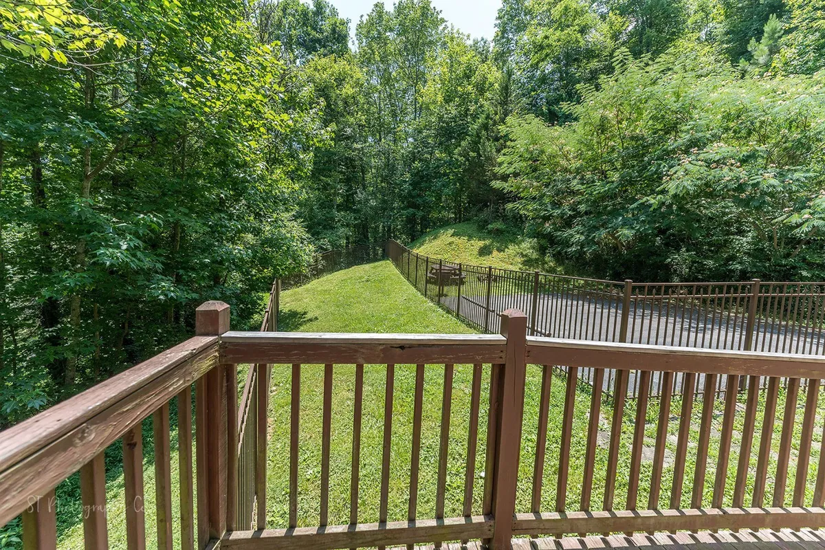 A peaceful pathway leads through verdant greenery beside a wooden deck railing, suggesting opportunities for outdoor exploration and activities like walking, grilling, and barbecues.