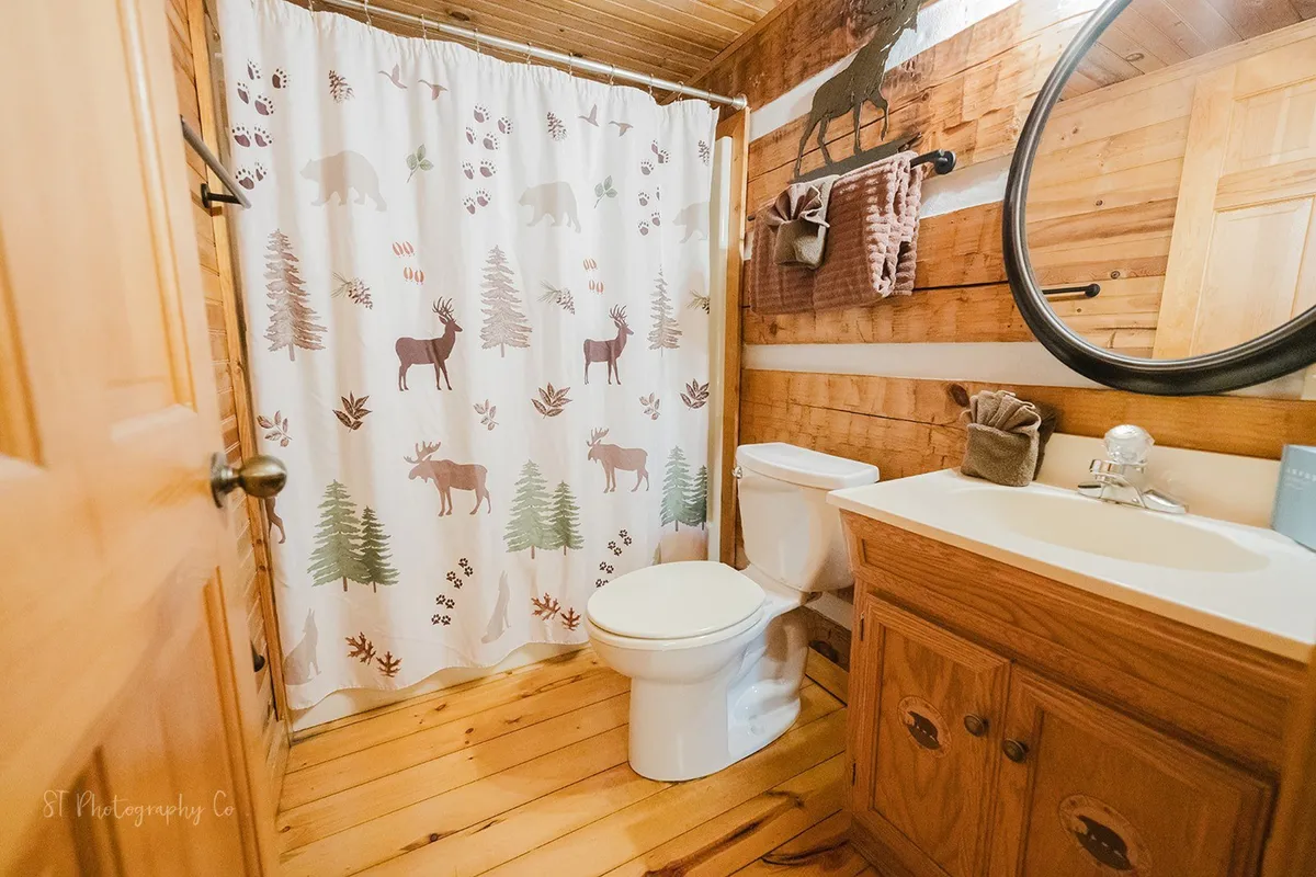 A warmly decorated bathroom with a shower curtain featuring animal motifs, wooden cabinetry, and a large mirror above the sink. The rustic touches create a welcoming space for personal relaxation and freshening up.