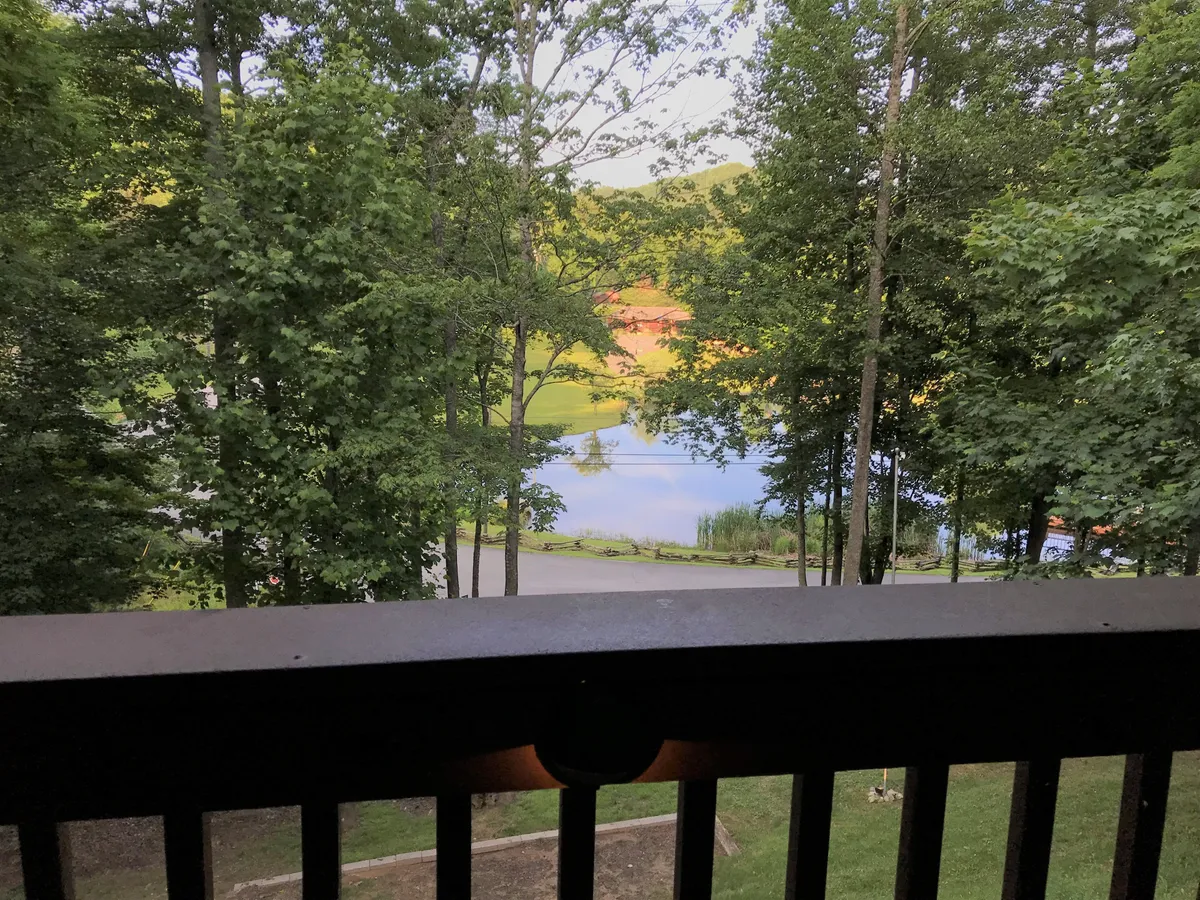 This image captures a serene view of lush greenery surrounding a calm pond, with distant hills in the background. The tranquil water invites visitors to fish, relax, or simply soak in the beauty of nature.