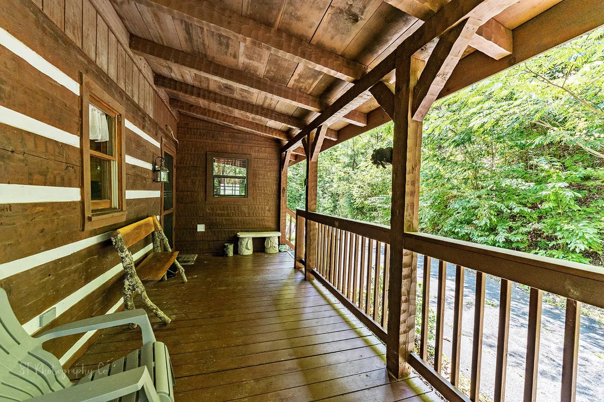 Cozy porch seating with wooden railings and beams frames a backdrop of lush forest, creating a serene spot perfect for enjoying the outdoors, relaxing with loved ones, or welcoming pets.