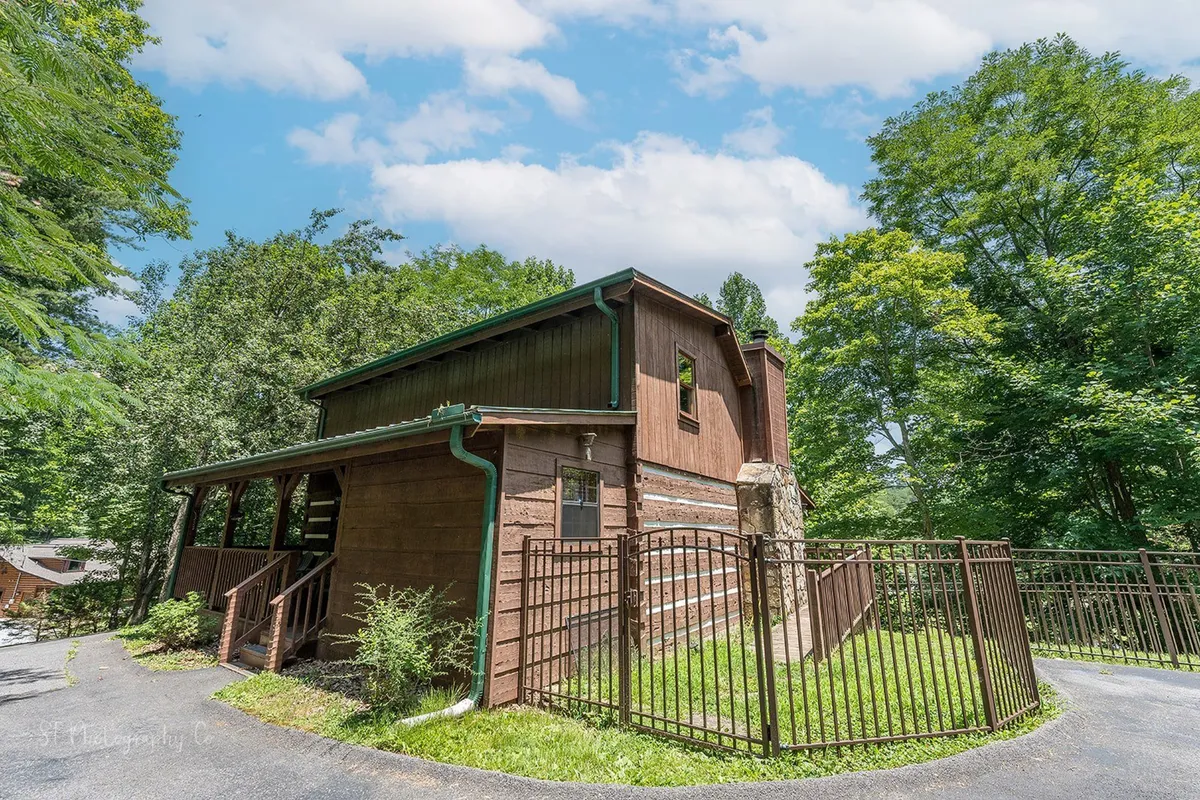 A view of the wooden cabin’s exterior featuring a fenced yard, landscaped greenery, and entrance stairs. The inviting porch and well-maintained outdoor space are visible, emphasizing the secure and spacious environment for families and pets.
