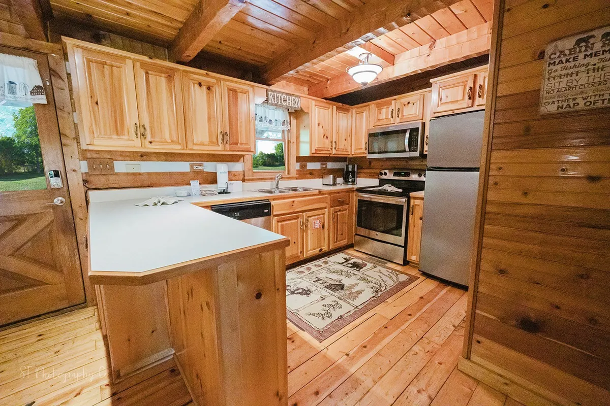 A close-up of the kitchen area, highlighting the warm wooden cabinetry, kitchen island, and stainless appliances. The decorative rug underfoot and coffee bar setup underscore the kitchen's functionality and cozy, homey appeal—the perfect place for meal prep, morning coffee, or a baking session.