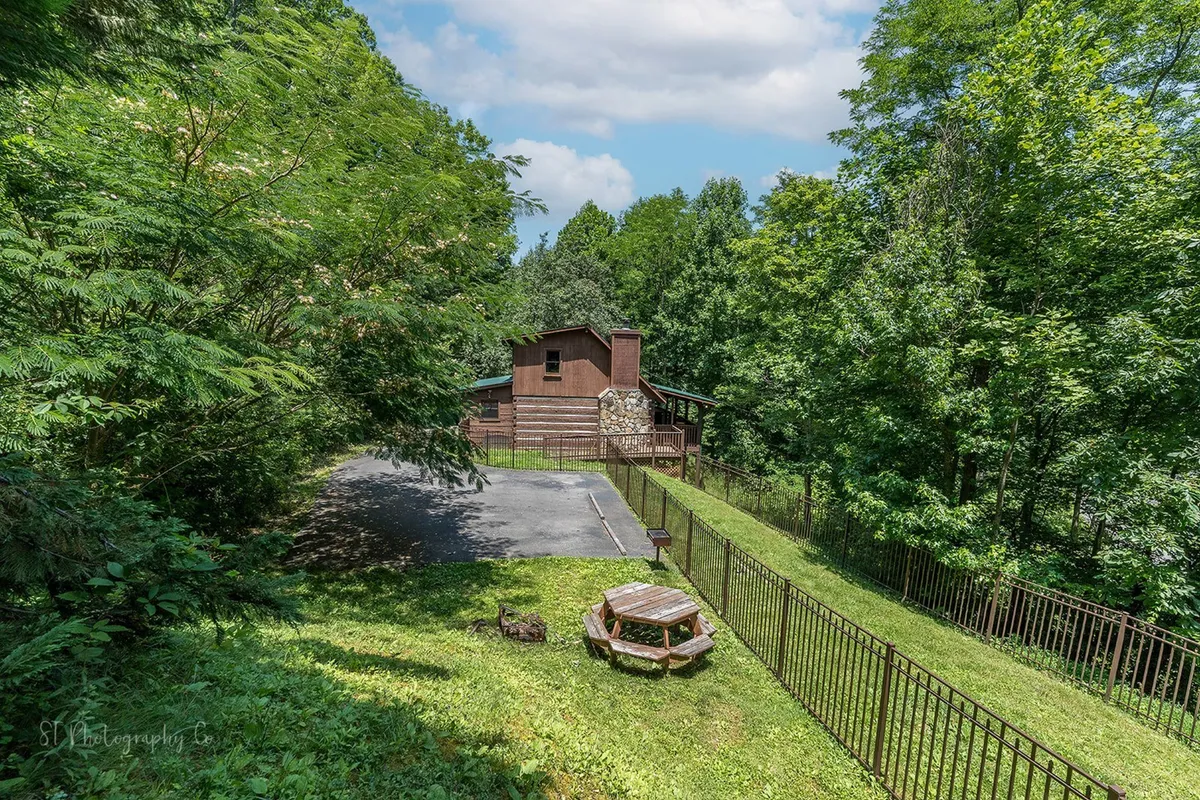 A broad view of the fenced yard with a picnic table prominently situated, surrounded by greenery and the house in the background. The space is clearly designed for outdoor dining and gatherings, offering safe play for children and pets within the fenced perimeter.