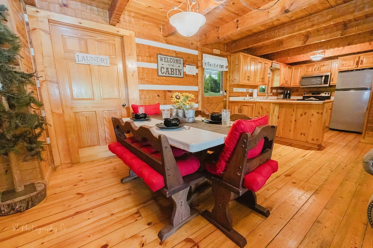 A focused shot of the dining nook with a wooden table, red cushion seating, a glimpse of the kitchen area, and a welcoming décor accent. The cozy setup encourages family meals, board games, and celebrations, capturing the spirit of gathering and shared experiences.