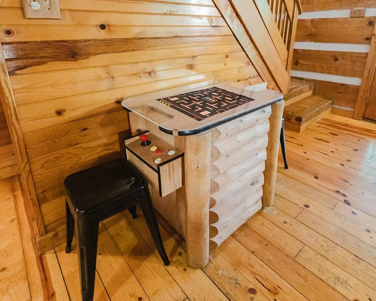 A nostalgic game nook featuring a classic arcade game table and wooden stools, surrounded by wood-paneled walls and a staircase. The inviting setup encourages friendly competition and shared laughter.