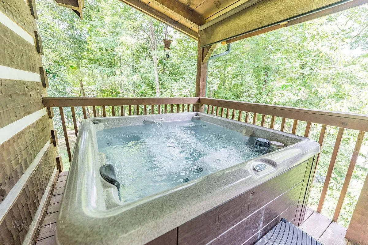 A serene outdoor scene with a hot tub set on a wooden deck surrounded by natural greenery. The tranquil setting emphasizes the amenities available for both guests and their pets after a day of exploring the nearby national park.